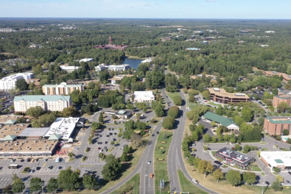 Suburban aerial view: roads, buildings, parking, dense trees.
